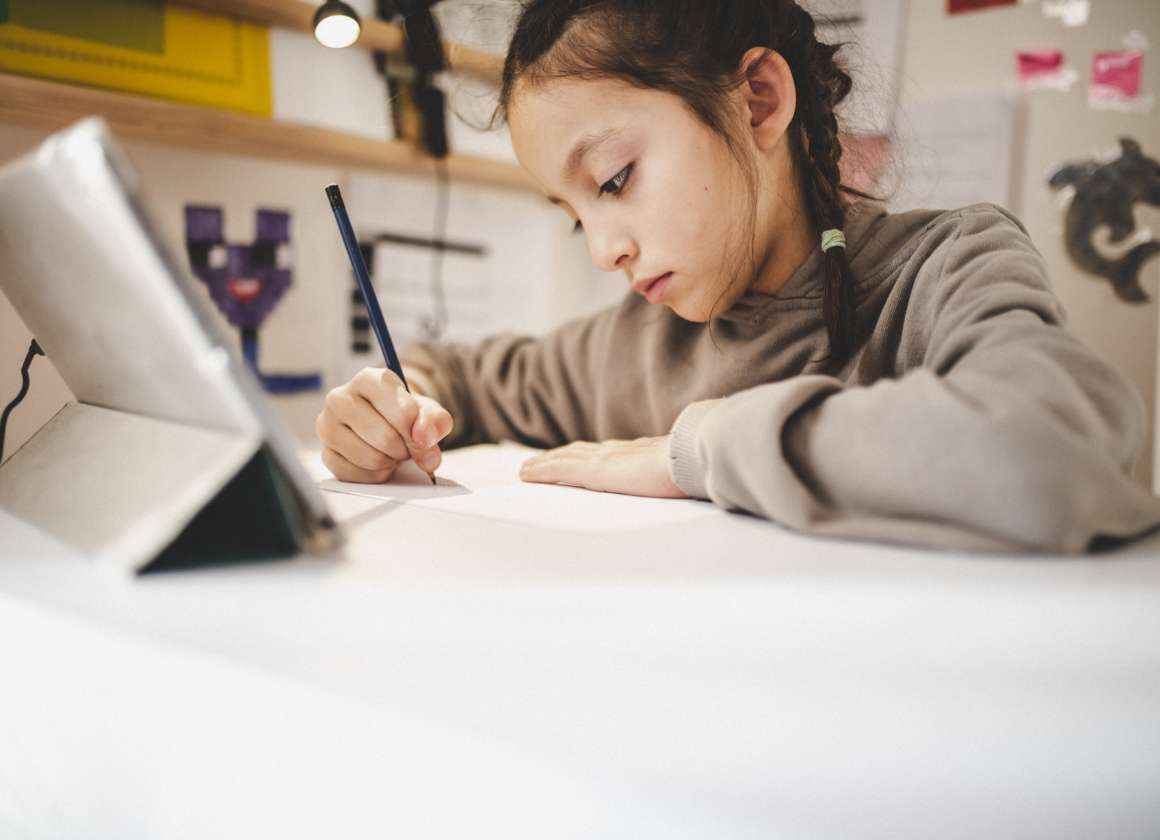 An image of a young person drawing at a desk looking at a tablet on a web page about Kids Help Phone’s mental health website