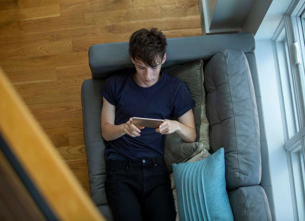 An image of a young person on a couch looking at a phone on a web page about Kids Help Phone’s mental health website